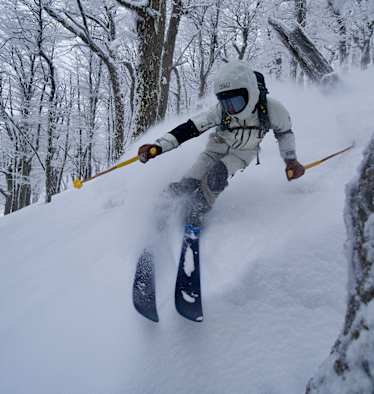 Freerider im Tiefschnee zwischen winterlichen Bäumen.