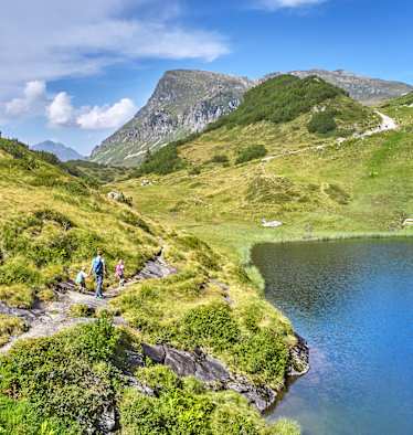 Drei Wanderer wandern an einem Bergsee entlang.