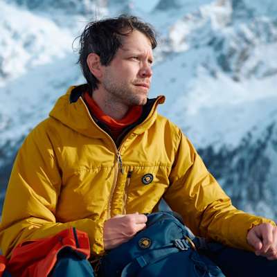 Mann in gelber Kunstfaserjacke sitzt in verschneiter Landschaft