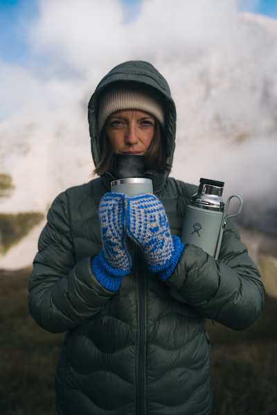 Person in Winterkleidung hält eine graue Hydro Flask Hot Flask & Cup in verschneiter Berglandschaft bei Nebel.