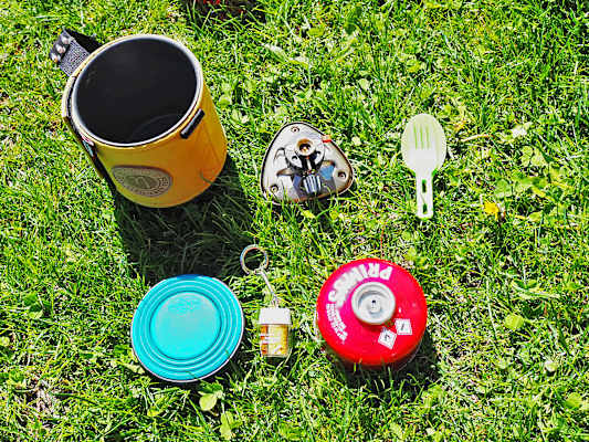 Kocher mit integrierter Kartusche, faltbarem Becher, Besteck und Gewürze.