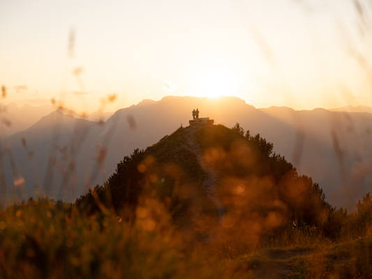 Zwei Personen bei einer Bank auf der Gratlspitze im Alpbachtal bei Sonnenuntergang.