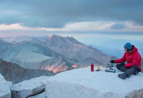 Mann kocht mit SOTO Kocher auf Berg Essen mit Panorama über Berge.