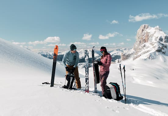 Eine Frau und ein Mann stehen im Schnee auf einem Berg und machen sich für das Skifahren bereit.