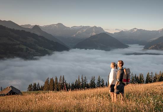 Zwei Wanderer genießen den Blick über ein Nebelmeer im herbstlichen Gstaad mit Bergpanorama im Hintergrund.
