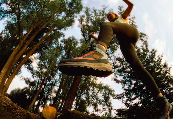 Frau springt im Wald über einen Baumstamm mit dem Hanwag Rotpunkt Light Mid GTX – leichter, vielseitiger Outdoor-Schuh für Alltag und Wanderungen