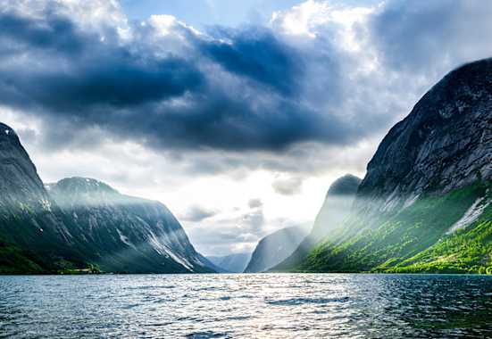 Norwegischer Fjord bei Sonnenaufgang mit schroffen Klippen und Wald 