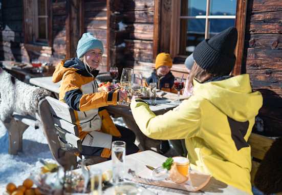 Zwei Damen stoßen mit einem Glas Wein auf der Skihütte im Winter an.