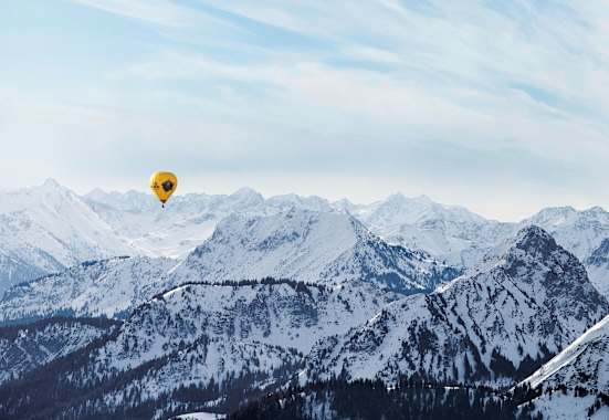 Ein gelber Heißluftballon, dahinter die schneebedeckten Alpen
