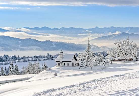 Die Hubertuskapelle in Scheidegg im Allgäu inmitten einer tief verschneiten Berglandschaft.
