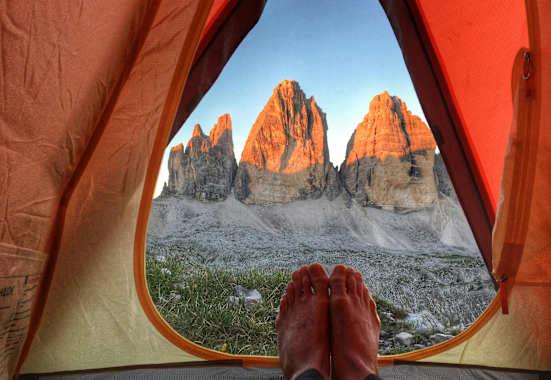 Ein Mann liegt in einem Zelt und genießt den Ausblick auf die Drei Zinnen.