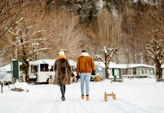 Ein Pärchen geht mit einem Rodel über einen Campingplatz im Winter.