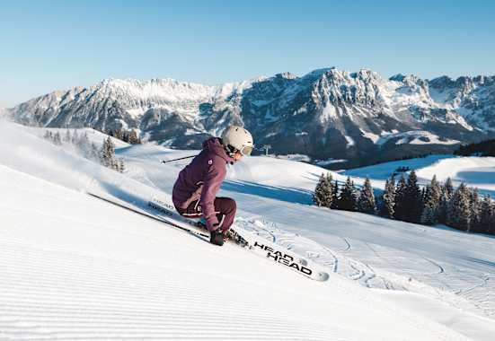 Eine Skifahrerin carvt im Skigebiet Wilder Kaiser- Brixental über eine frisch präparierte Piste. Im Hintergrund die markante Bergkulisse des Wilden Kaisers.