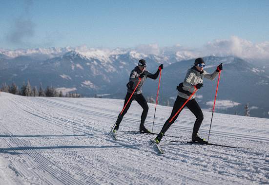 Zwei Langläufer auf einer Loipe in der neuen Nordic Kollektion von Löffler.