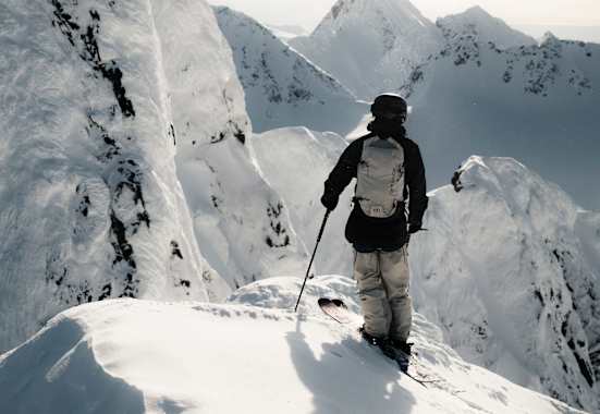 Ein Freerider steht auf einem Hang und blickt den verschneiten Berg hinab.
