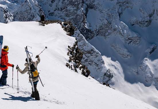 Auf einem schneebedeckten Hang stehen zwei Skitourengeher und zeigen in die Ferne. Sie sind mit der Bergtagen-Kollektion von Fjällräven ausgerüstet.