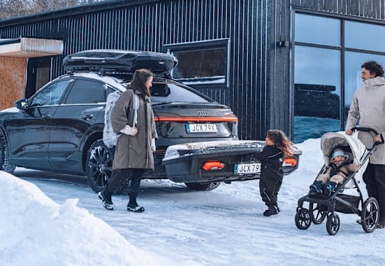 Eine vierköpfige Familie steht vor ihrem Auto, auf dem eine Thule-Heckbox befestigt ist.