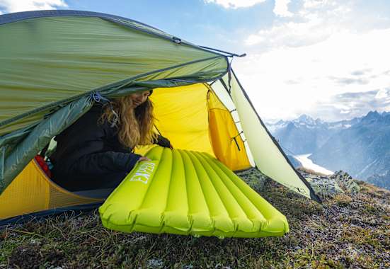 Eine Frau sitzt in einem Zelt und zieht eine Schlafmatte von Exped hinein.