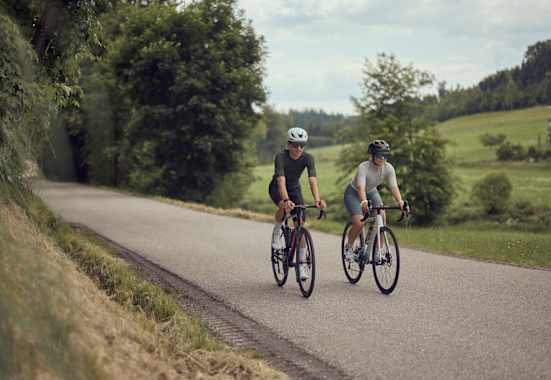 Zwei Radfahrer fahren auf einer ruhigen Landstraße im Mühlviertel bei der Bike Experience, umgeben von grüner Natur und sanften Hügeln.