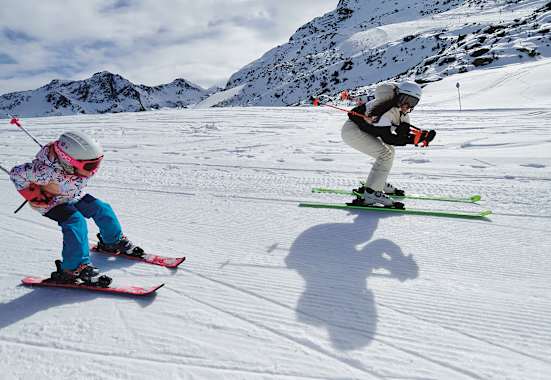 Eine Frau und ein Mädchen fahren gemeinsam Ski und nehmen dabei die Schussposition ein.