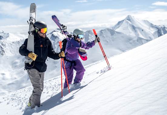 Ein Skifahrer und eine Skifahrerin gehen eine Piste in Ischgl hinauf.