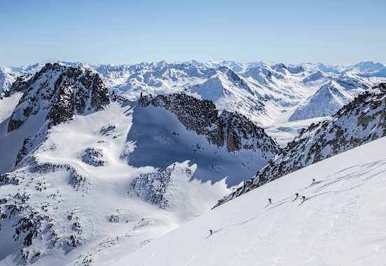 Markante Felsen die vom Schnee bedeckt sind. Skitourengeher fahren einen unverspurten Hang hinunter.