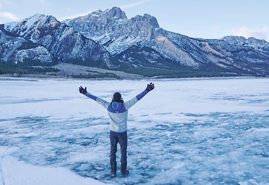 Ein Mann steht vor einem Berg im Schnee mit offenen Armen.