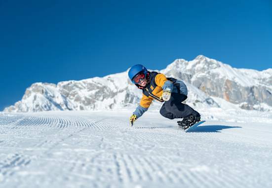 Ein Kind fährt in Snowboardbekleidung im Winter die Piste herunter.