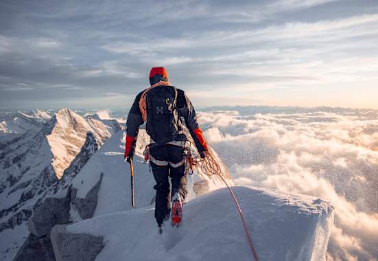 mann beim bergsteigen auf bergspitze, gekleidet in haglöfs