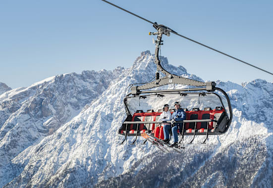 Ein Skilift in den verschneiten Bergen mit 2 Personen, die drinnen sitzen.
