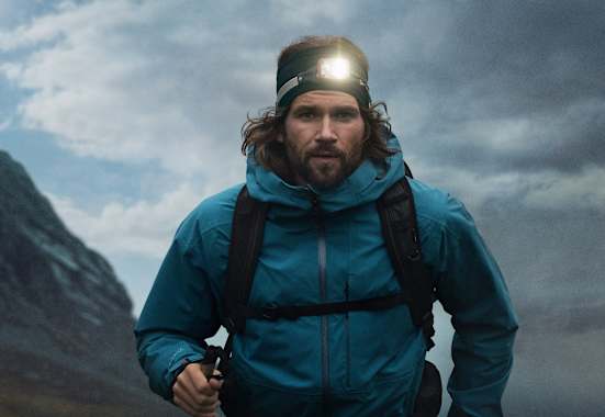 Ein Mann mit einer leuchten Stirnlampe geht mit Wanderausrüstung