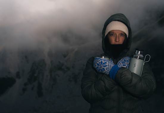 Person in Winterkleidung mit Thermosflasche Hydro Flask Hot Flask & Cup in verschneiter Berglandschaft bei Nebel und eisigen Temperaturen.