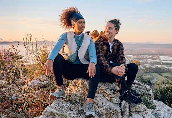 Zwei Frauen sitzen auf einem Fels in den Bergen.