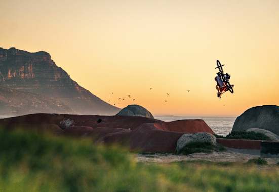 BMX-Biker dreht sich in Luft vor Küstenszenerie.
