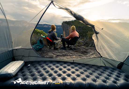 Sea to Summit Isomatte und Kissen im Zelt mit Blick auf zwei Camper, die den Sonnenuntergang in den Bergen genießen