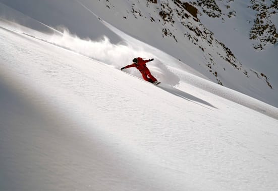 Eine Person fährt Snowboard im Schnee auf einem Berg in roter Ausrüstung.