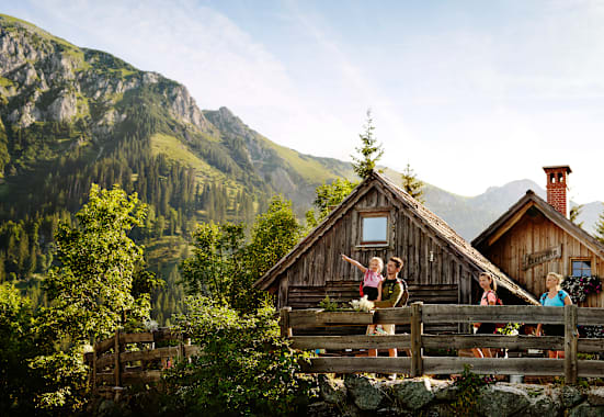 Eine Familie mit 2 Kindern steht auf einer Bergalm in der Steiermark im Sommer und beobachtet die Umgebung.