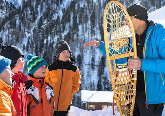 Der Kursleiter Peter zeigt und erklärt den Kindern einen alten Schneeschuh.