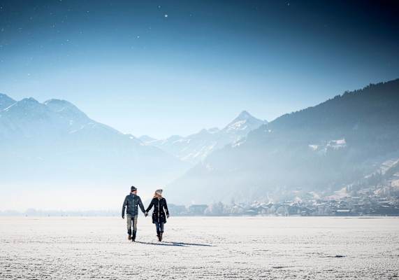 Spaziergeher am gefrorenen Zeller See, im Hintergrund das Kitzsteinhorn