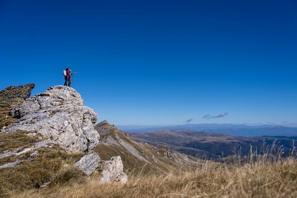 Wandern im Dinarischen Gebirge; zwei Wanderer genießen die Aussicht über sanfte Berggipfel