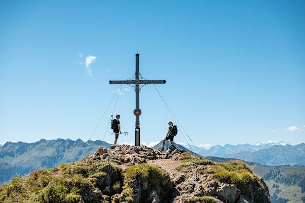 Zwei Personen stehen direkt am Gipfelkreuz der Gratlspitze im Alpbachtal, die eine weite Aussicht bietet.