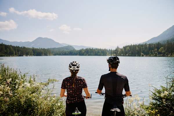 Zwei Radfahrer stehen am Ufer des Hintersees bei Ramsau im Berchtesgaden und blicken über den See.