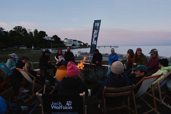 Eine Gruppe von Menschen sitzt um ein Lagerfeuer am Strand auf Rügen - die Fahne von Jack Wolfskin und dem Wolf Trail ist im Hintergrund zu sehen.