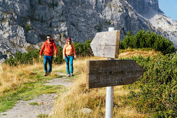 Zwei Wanderer auf der Karnischen Milchstraße und ein Wanderschild aus Holz im Vordergrund.