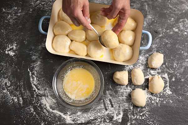 Buchteln (Wuchteln, Rohrnudeln) werden in eine Backform gesetzt und mit Ei bepinselt