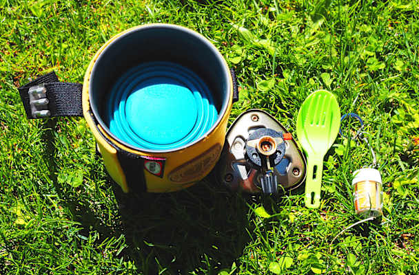 Kocher mit integrierter Kartusche, faltbarem Becher, Besteck und Gewürze.