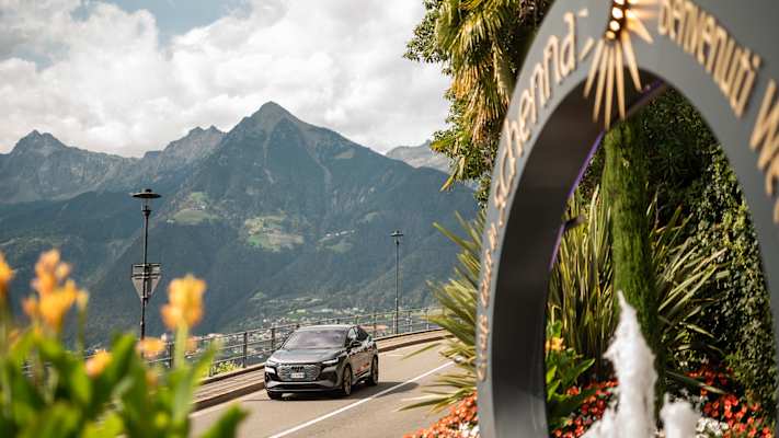 Ein modernes Auto auf der Straße, die nach Schenna führt, im Hintergrund die Bergwelt.