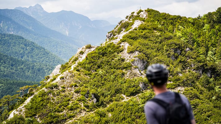 Ein Biker steht vor einer Kulisse aus Bergen und Naturpanorama.