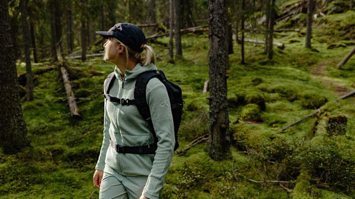 Frau im grünen Wald mit Kappe und türkiser Kleidung.
