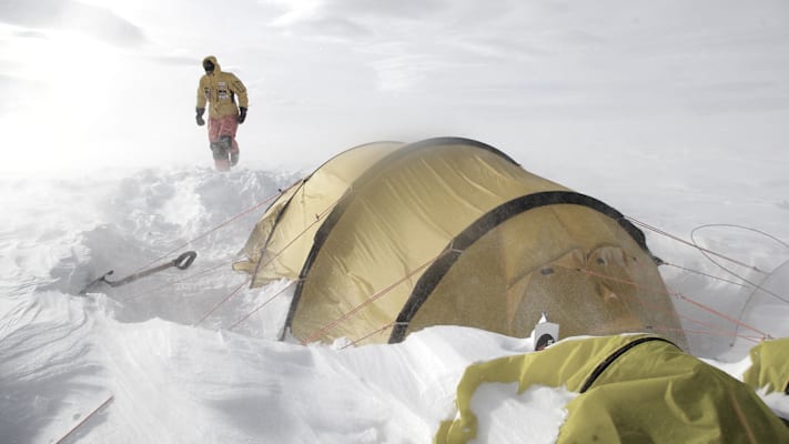 Ein Mann stapft durch Schnee und Eis zu seinem Zelt.